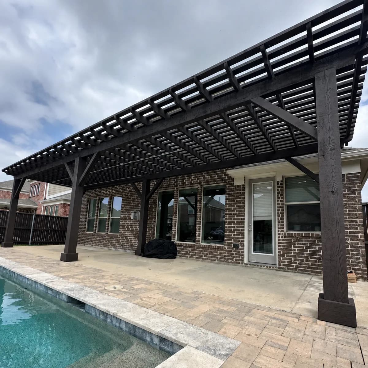 A 40 foot dark-stained cedar pergola running the length of a house above a poolside walk in Waxahachie