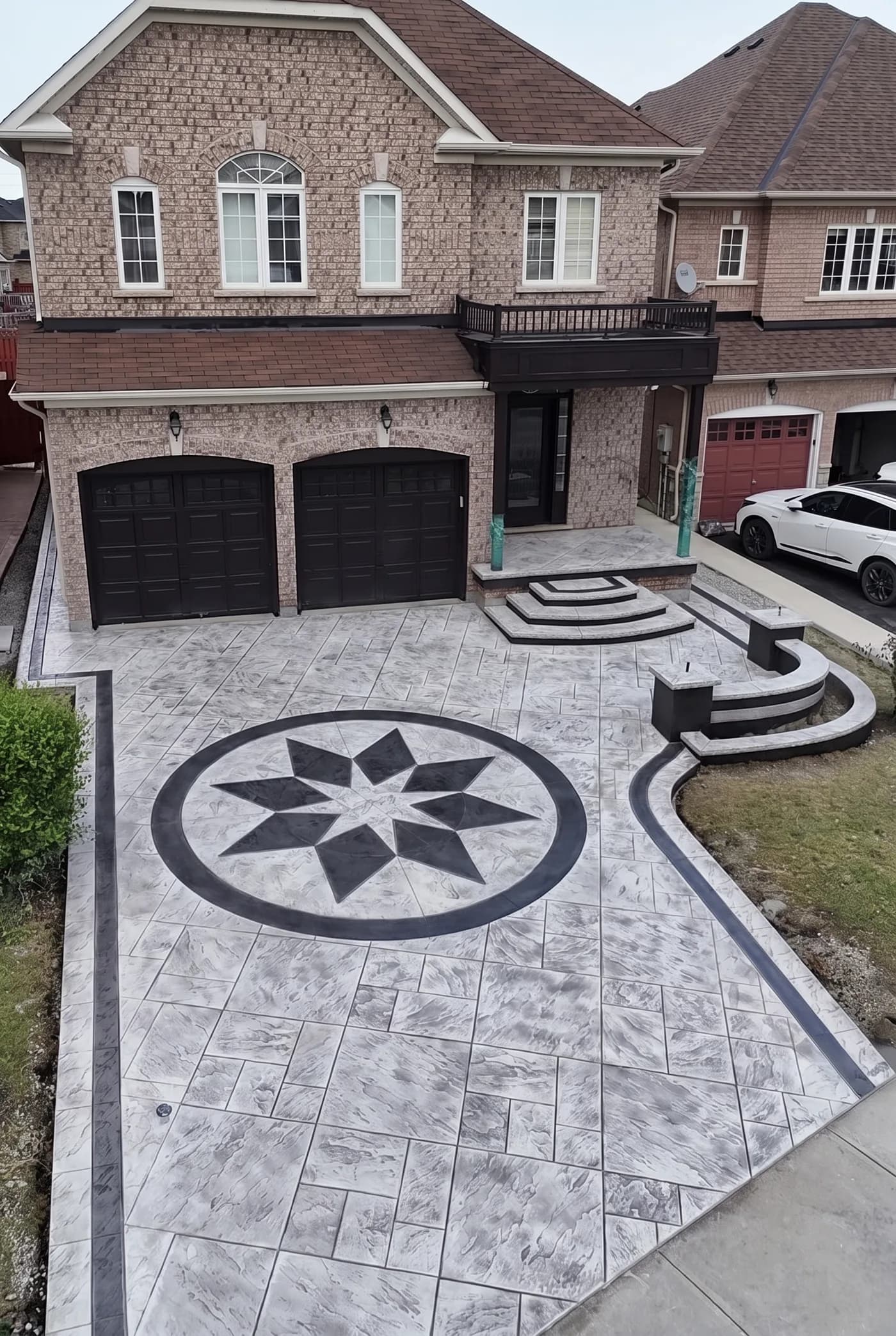 Aerial view of a stamped concrete driveway with a compass-star medallion inlay and dark contrasting borders in front of a brick home