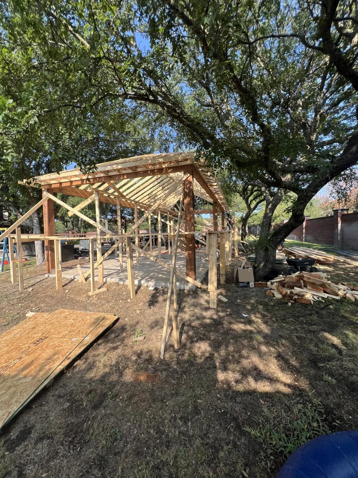 Cedar pavilion framing going up under mature oaks on a Royal Patio jobsite