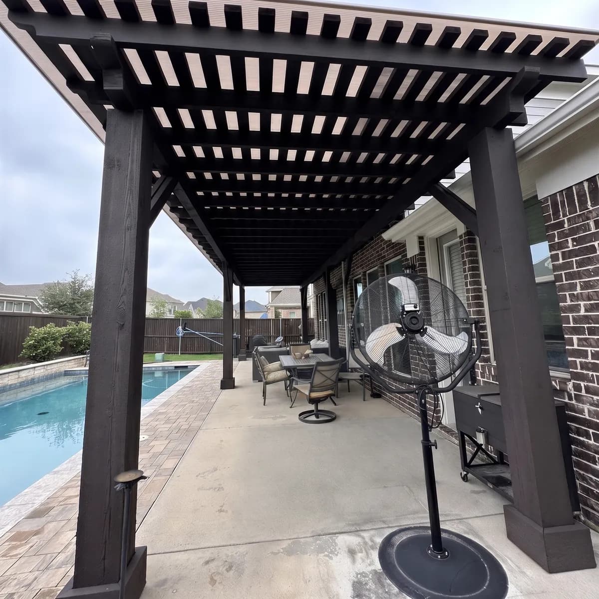 The underside of a full-length dark-stained Royal Patio pergola beside a pool
