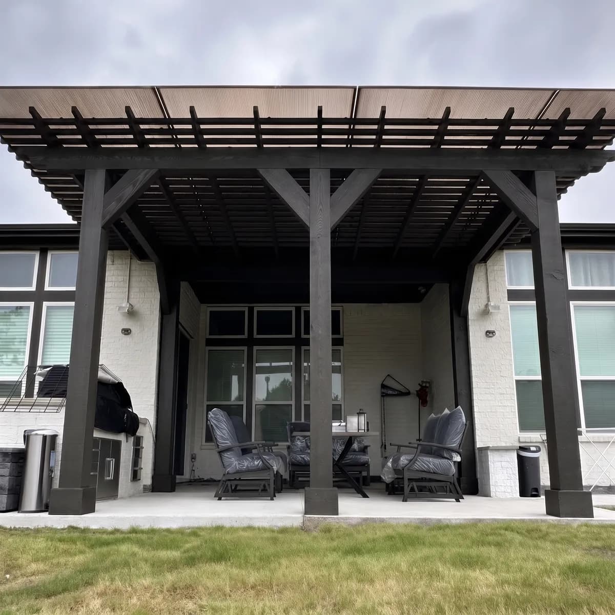 A dark-stained covered cedar pergola built by Royal Patio over an outdoor kitchen
