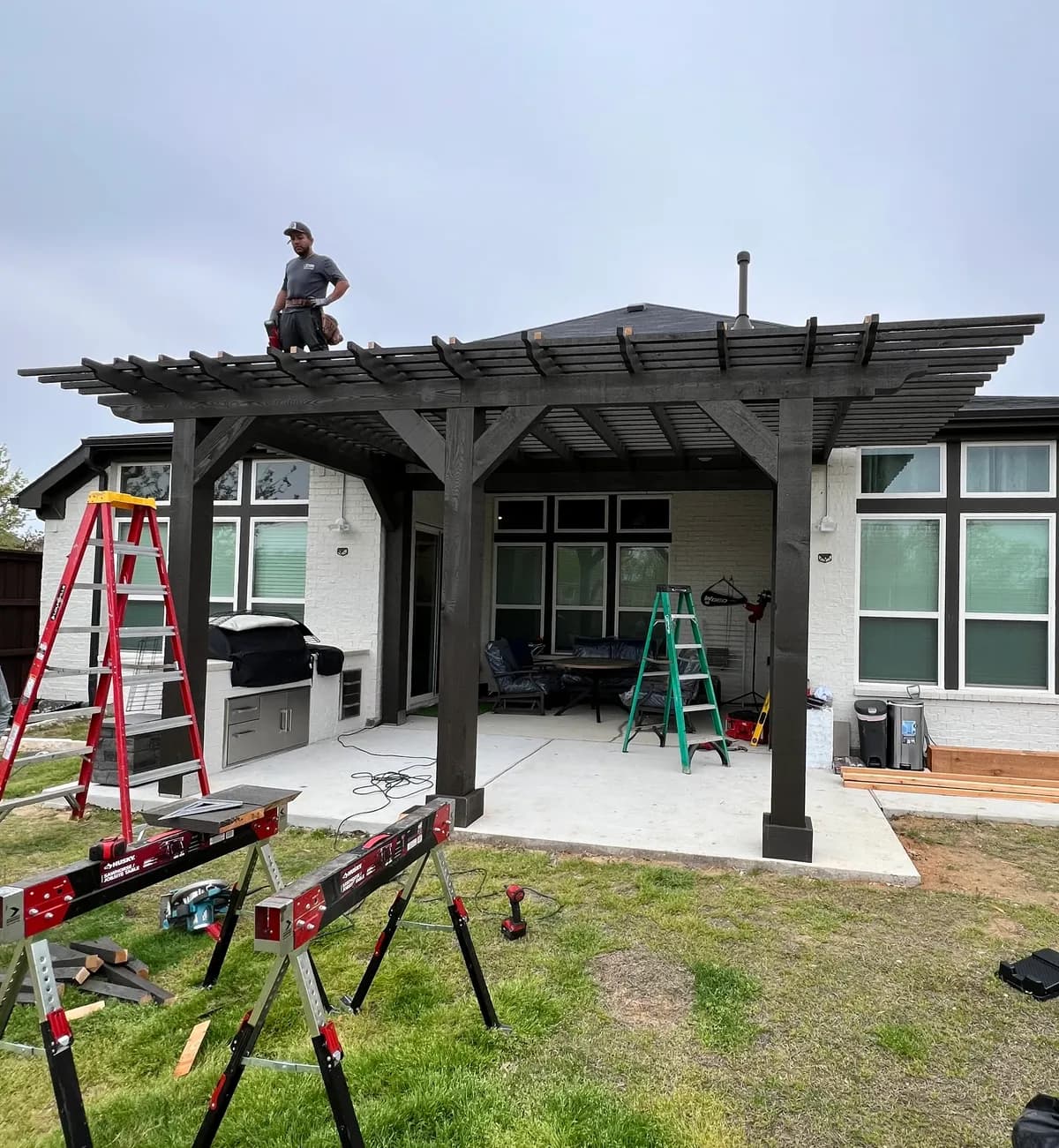 A Royal Patio crew member standing on the roof deck of a dark-stained pergola during the build of an Allen outdoor kitchen project