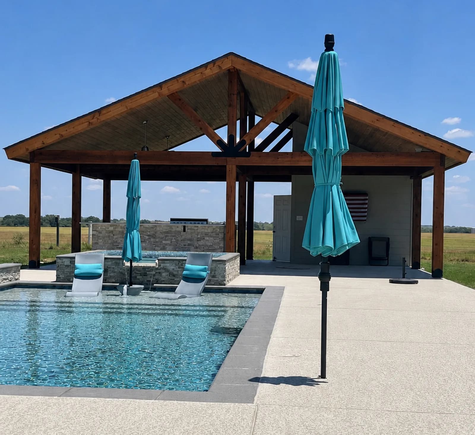 A gabled cedar patio cover with exposed trusses over a poolside cabana, spa, and outdoor kitchen under a blue Texas sky